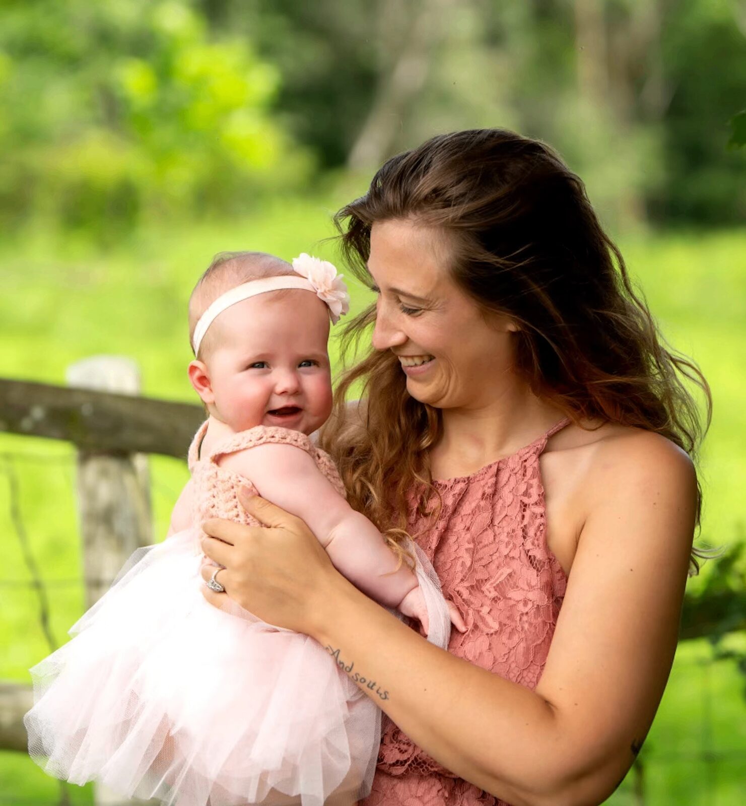Chrissy smiling and holding her baby daughter in a tutu outdoors